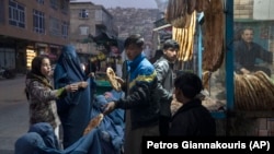 A man distributes bread to burqa-wearing women outside a bakery in Kabul in December.