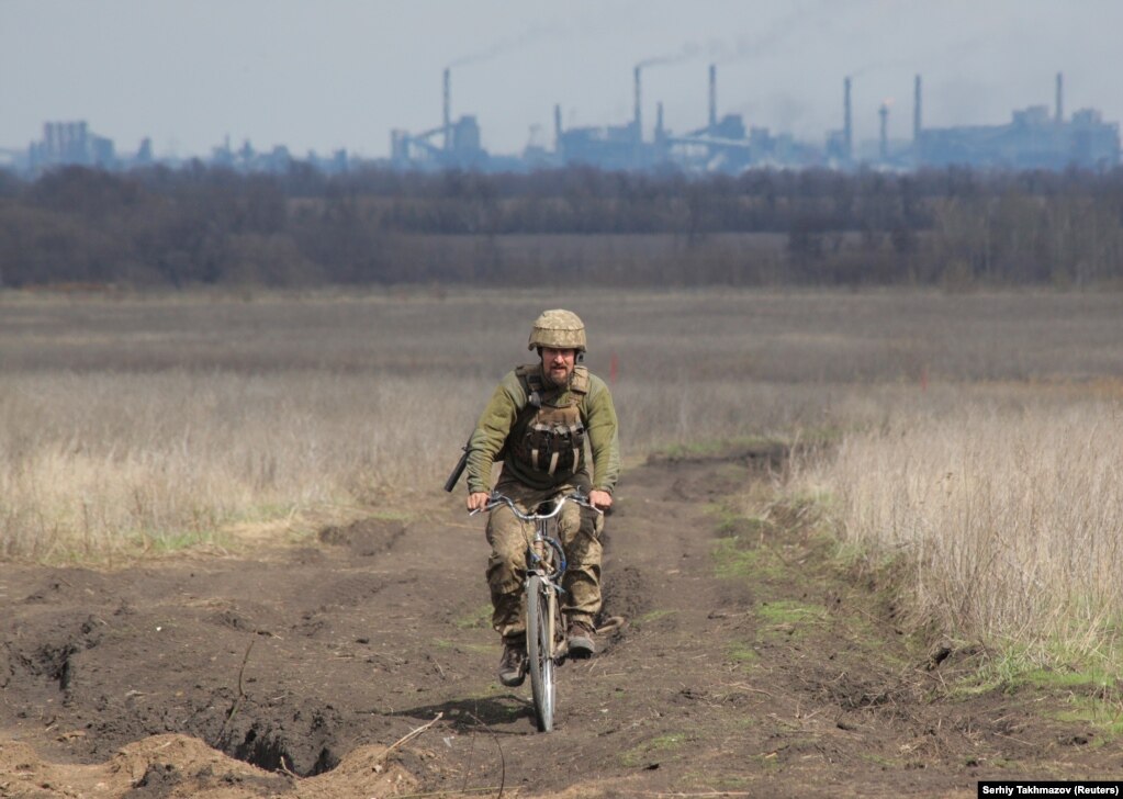 Një pjesëtar i forcave të armatosura ukrainase, duke ngarë një biçikletë, në pozicionet e luftimit, në vijën e ndarjes, pranë qytetit të Donetskut, që kontrollohet nga rebelët, teksa fabrika për prodhimin e koksit, Avdiivka, shihet në prapavijë, afër Donetskut, në Ukrainë. (17 prill)