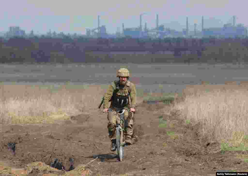 Припадник на украинските вооружени сили, вози велосипед, на борбени позиции, на линијата на поделба, во близина на градот Доњецк, кој е под контрола на бунтовниците, додека во позадина се гледа фабриката за кокс Авдиивка, во близина на Донецк, во Украина. 17 април 2021.