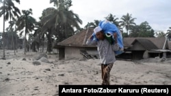 یک روستایی در حال حمل باروبنه خود پس از فوران آتشفشان کوه سِمِرو که خانه‌ها را در زیر تلی از خاکستر مدفون کرده است.