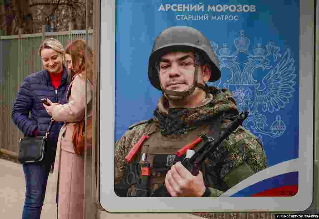 Women stand at a bus stop next to an advertisement for military conscription showing a Russian soldier, in Moscow.