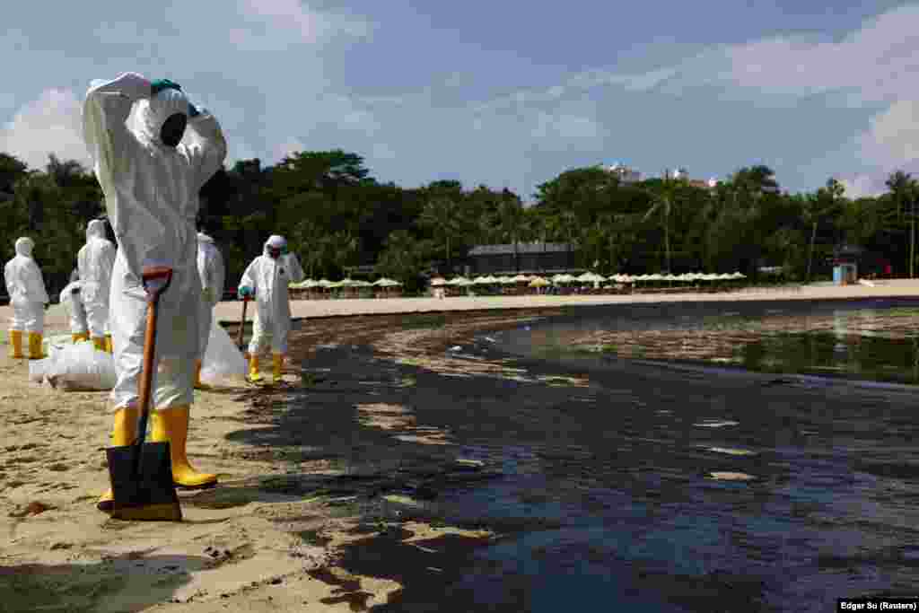 Punëtorët bëjnë një pushim të shkurtër gjatë punës për pastrimin e plazhit nga nafta e derdhur. Derdhja e naftës u shkaktua nga një incident detar kur një anije që shërben për pastrim dhe gërmim goditi një anije bunker në terminalin Pasir Panjang më 14 qershor.