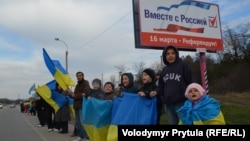 Крымчане с детьми держат украинские флаги на фоне билборда с призывом голосовать за присоединение к России, протестуя против проведения псевдореферендума в Крыму. Окрестности Бахчисарая, Крым, 14 марта 2014 г.