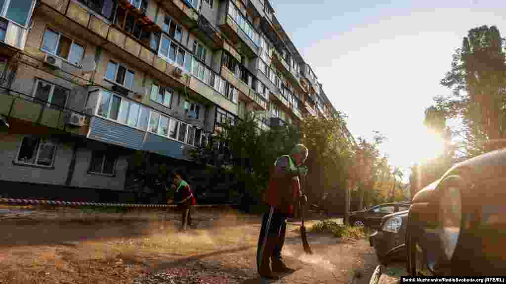 Муніципальні служби прибирають територію перед житловим будинком, пошкодженим під час російської атаки Києва 1 червня 2023 року
