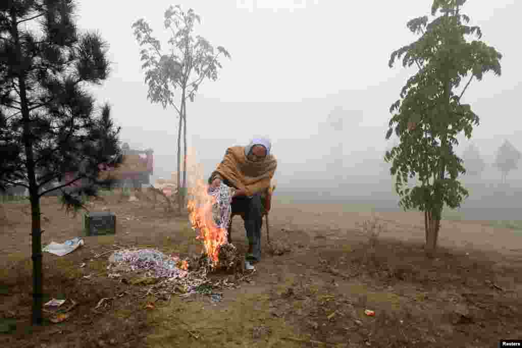 له پېښور سره نېږدې یو کس په یخنۍ او لړه کې د ځان تاوده ساتلو لپاره کاغذونه سوځوي - د جنورۍ نهمې انځور.