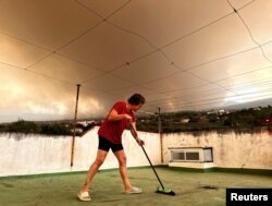 Hozefina Mingiljon (62) čisti pepeo sa balkona svoje kuće dok se dim diže u daljini, Tenerife, Španija, 19. avgust 2023.
