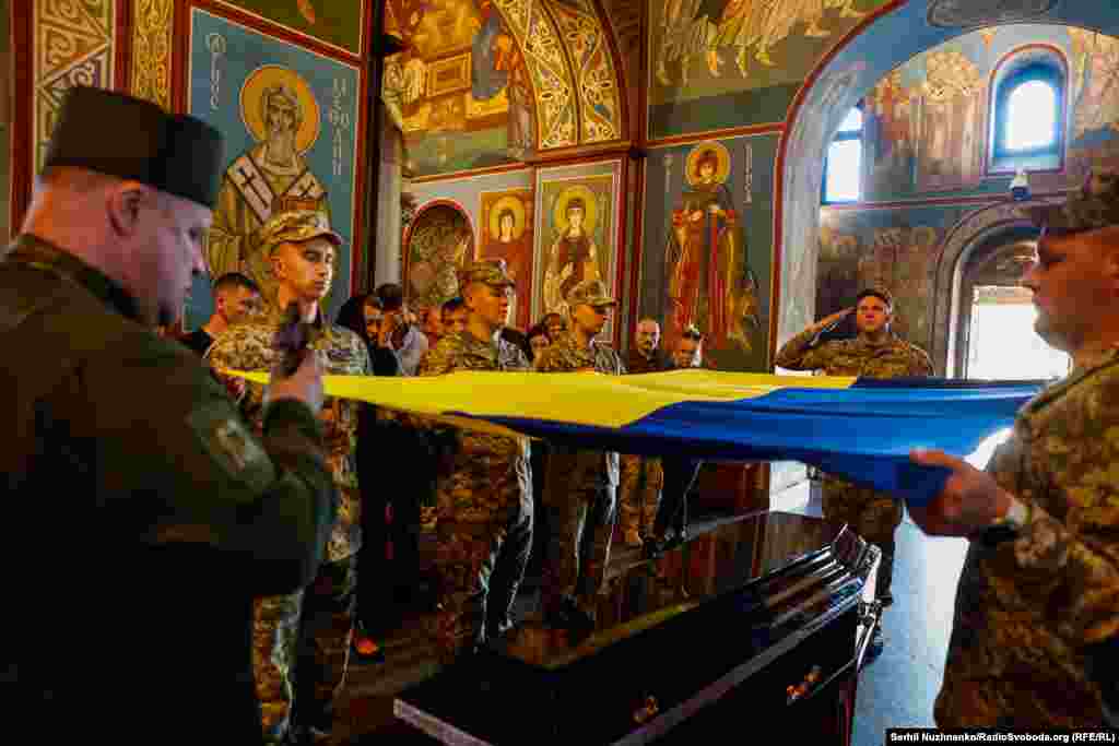 Soldați ridică drapelul ucrainean în timpul unei ceremonii de adio organizate la Catedrala cu Domul de Aur Sfântul Mihail din Kiev, la 18 iunie, pentru colonelul Valentin Korenciuk, un pilot de luptă - și una dintre &quot;Fantomele Kievului&quot; - care a fost ucis în aprilie în timpul unei misiuni.