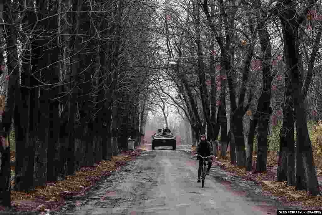 A man cycles as a military infantry vehicle drives through the town of Chasiv Yar, near the front line in Ukraine&#39;s Donetsk region.