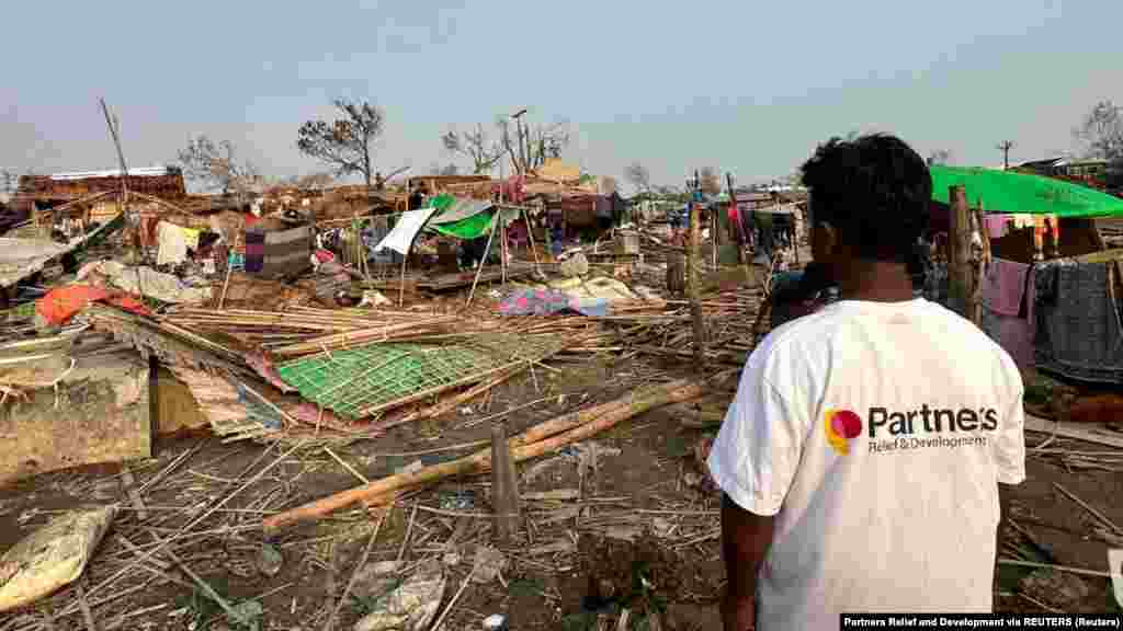Një burrë me një bluzë me logon e organizatës Partners Relief and Development duke shikuar dëmet e shkaktuara nga cikloni Mocha në Sitve, Mianmar. Fotografitë u publikuan më 17 maj 2023. Stuhia e fuqishme goditi brigjet e Bangladeshit dhe Mianmarit më 14 maj.