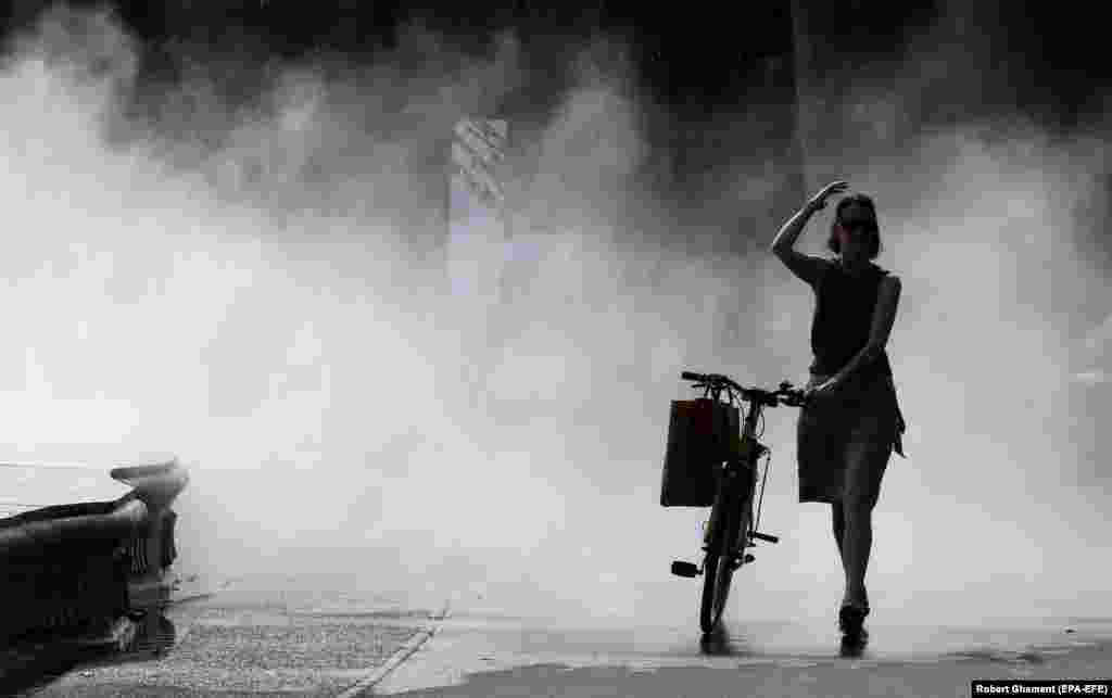 A woman cools off while passing through water mist during a hot summer&#39;s day in Bucharest.