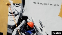 A worker in St. Petersburg paints over a mural depicting jailed Russian opposition politician Aleksei Navalny in April 2021. The lettering reads: "The hero of the new age."