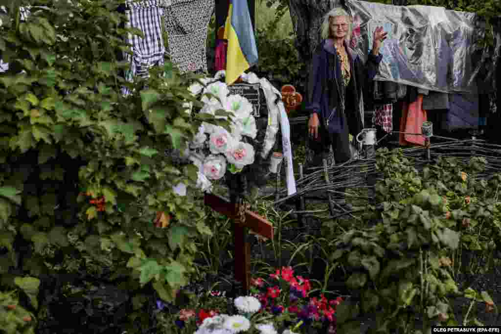 60-летняя Ирина смотрит на могилу сына Романа. Он похоронен в саду возле дома в селе Долгенькое на востоке Украины. Роман погиб в результате российского обстрела. Ему было 39 лет