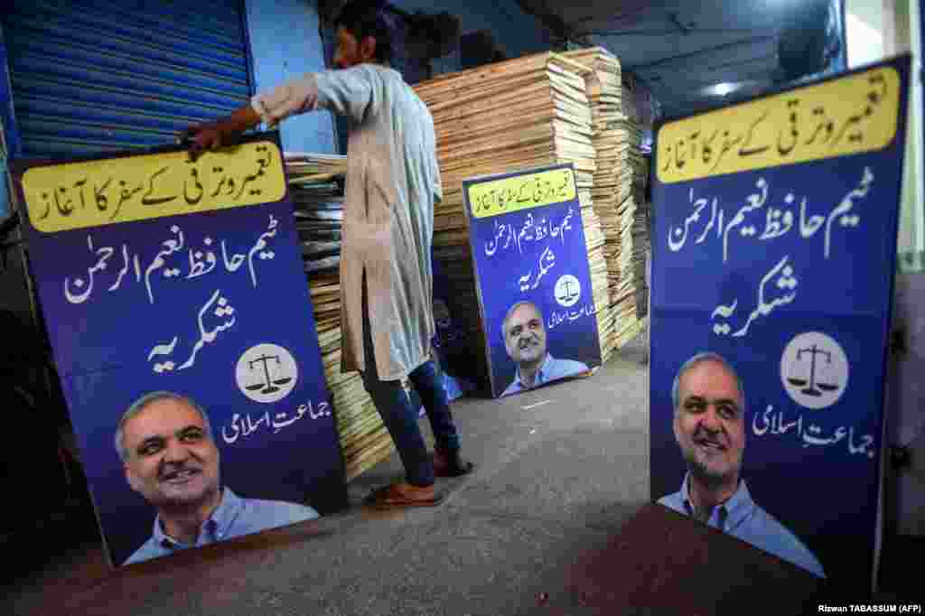 A worker arranges the posters of the Jamaat-e Islami (JI) party in Karachi, featuring their leader Hafiz Naeem ur-Rehman and the symbol of a scale.