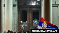 Поддржувачите на опозицијата се собираат пред зградата на градскиот совет на Белград додека полицајците стојат зад вратите на градскиот совет за време на протестот во Белград, на 24 декември 2023 година