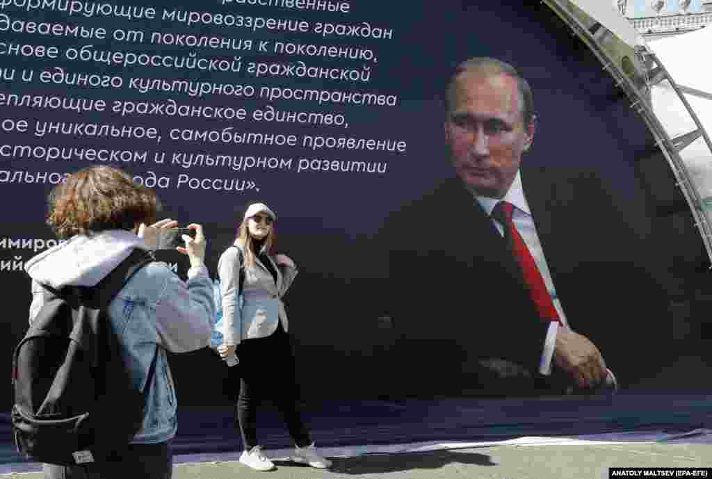 A woman has her picture taken in front of a portrait of Russian President Vladimir Putin during a book fair on the Dvortsovaya (Palace) Square in St. Petersburg.