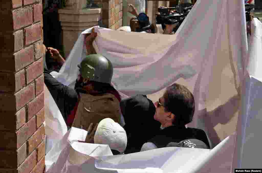 Former Pakistani Prime Minister Imran Khan and his wife, Bushra Bibi, are covered with a white sheet as they arrive to appear at the High Court in Lahore, Pakistan, on May 15.&nbsp;