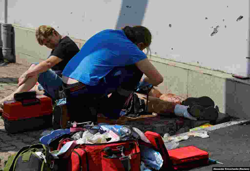 A paramedic treats an injured person as another woman waits for treatment.