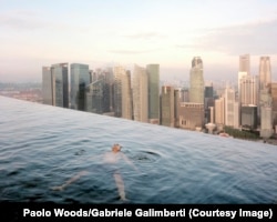 Un bărbat plutește în piscina de la etajul 57 a Hotelului Marina Bay Sands, cu linia orizontului din „Central", districtul financiar din Singapore, în fundal.