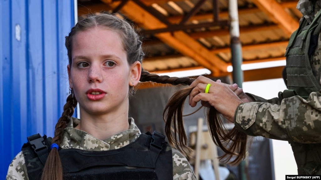 Një kadete ukrainase, e veshur në uniformën e re ushtarake, duke i gërshetuar flokët. &nbsp;