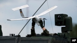 Войник държи дрон над военен автомобил на НАТО по време на военно учение в Литва през юни 2023 г.