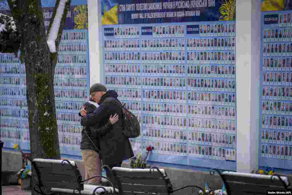 People hug next to the Memory Wall commemorating fallen Ukrainian military members in Kyiv.