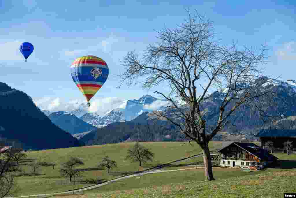 Dy balona me ajër të nxehtë duke fluturuar mbi Gstaad, pranë Chateau-d&#39;Oex në Zvicër.