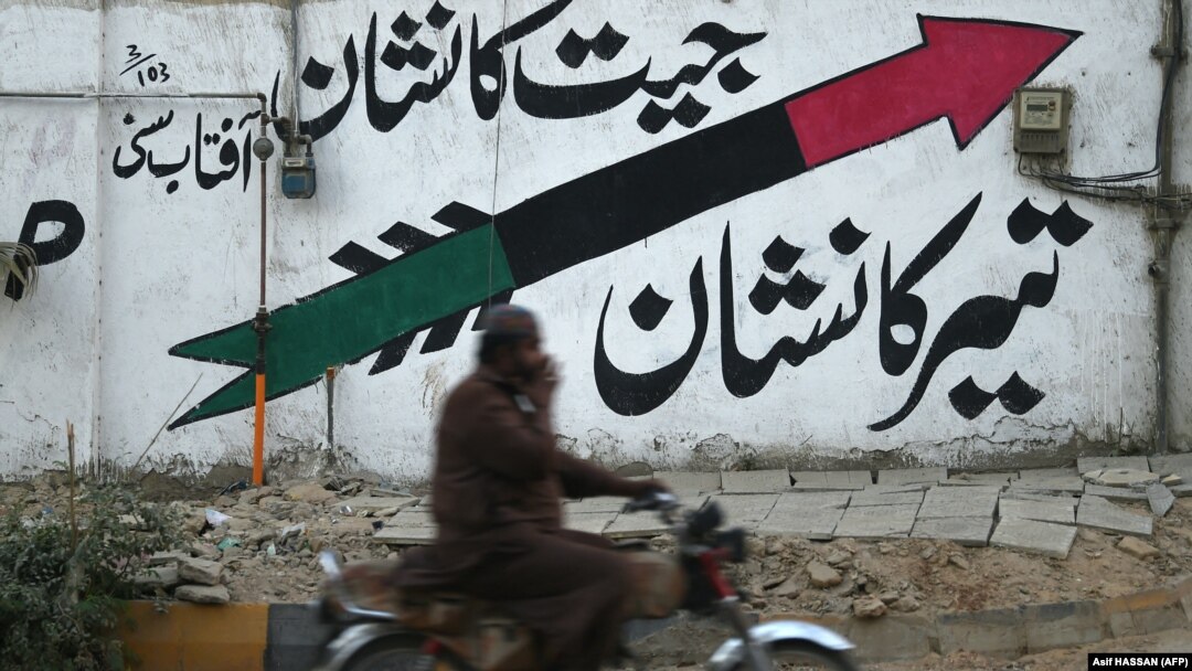 Un bărbat pe motocicletă trece pe lângă un zid pictat cu logo-ul Partidului Popular Pakistanez (PPP) pe o stradă din Karachi, 12 ianuarie 2024.