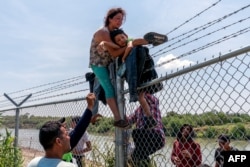Нелегальные мигранты перелезают через забор на пограничной реке Рио-Гранде в США, штат Техас. 25 августа 2023 года