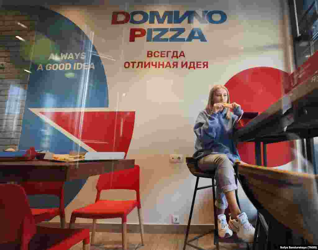 O femeie savurează o felie într-o unitate Domino&#39;s Pizza din Moscova, redeschisă pe 30 august sub numele de &quot;Domиno Pizza&quot;, cu &quot;i&quot; latin din nume înlocuit cu litera chirilică echivalentă &quot;и&quot;.