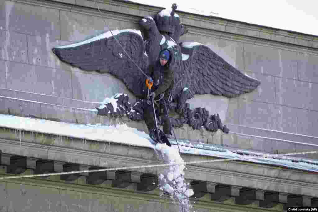A worker clears snow from the facade of the building of the Central Bank of Russia, decorated with a bas-relief of a double-headed eagle, the coat of arms of Russia, in St. Petersburg on March 30.