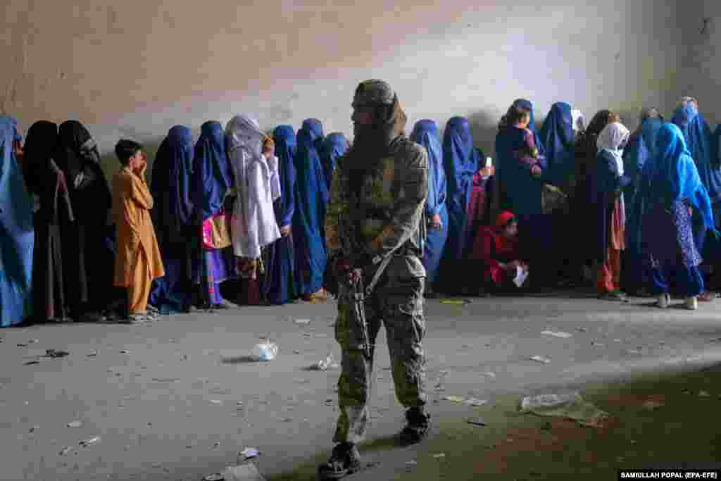 A Taliban fighter stands guard as Afghans wait in line to receive aid rations in Kabul.