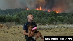 Un polițist grec evacuează un copil dintr-un incendiu de vegetație în satul Agios Charamlabos, în apropiere de capitala Atena, pe 18 iulie 2023.