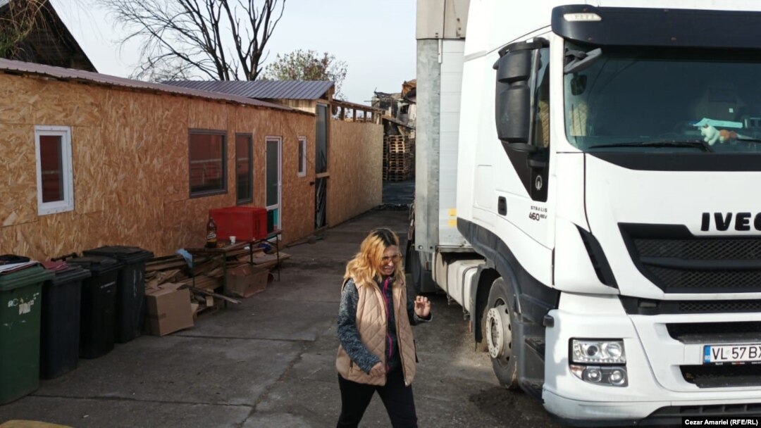 Un camion descarcă marfă în curtea familiei sinistrate Iliescu din Crevedia. În stânga, adăpostul improvizat din containere, în care locuiesc după explozie cei zece membri ai familiei. Pe fundal se văd ruinele casei.