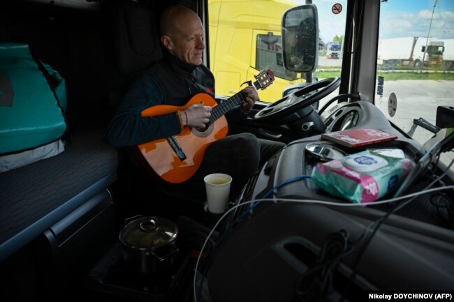 Shoferi Gediminas Gostautas luan me gitarë teksa pret në kufirin mes Bullgarisë dhe Rumanisë më 24 mars 2024.