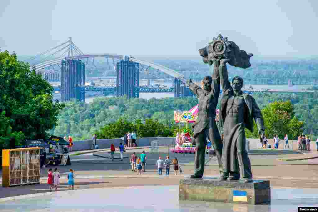 Две централни фигури от съветския комплекс, посветен на прославата на повторното обединение на Украйна и Русия в центъра на Киев. Статуята изобразява руски и украински работници, обединени под емблемата на Съветския съюз. Статуята беше свалена през април 2022 г. &nbsp;Месец по-късно комплексът, над който се издига и голяма метална арка, беше преименуван в Арка на свободата на украинския народ.