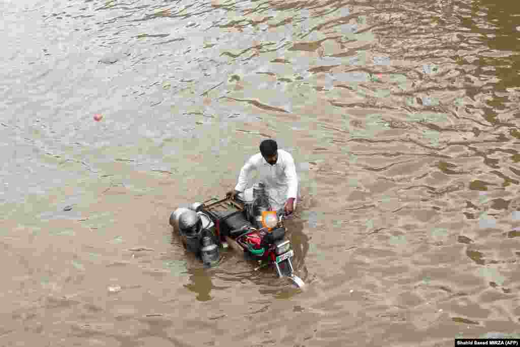 In Multan, Punjab Province, a milkman pushes his motorcycle through floodwaters following intense monsoon rains.