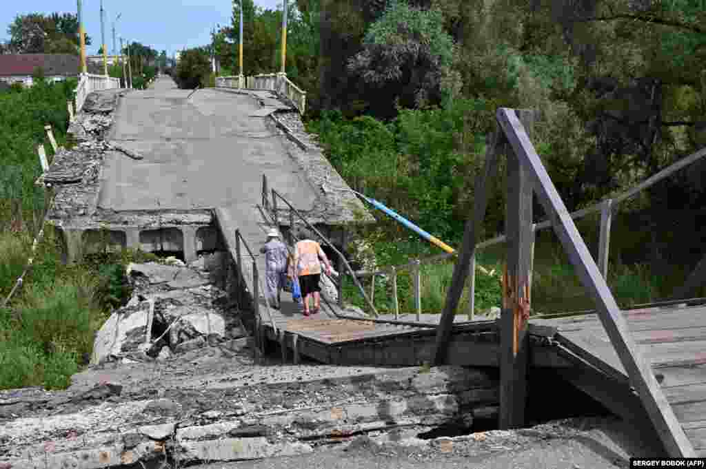 Ljudi hodaju po porušenom mostu u Vovčansku u ukrajinskoj oblasti Harkiv.