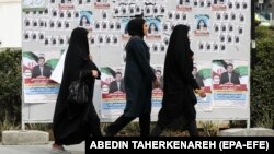 İranlı qadınlar qarşıdan gələn parlament seçkilərində iştirak edən namizədlərin seçki plakatlarının yanından keçir.