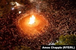 Krugovi plesača kruže oko vatre dok se tradicionalna muzika izvodi s glavne pozornice događaja (dolje desno).