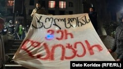 საპროტესტო ბანერი პარლამენტის შენობასთან, რომელიც აქციის მონაწილეებმა გაშალეს წულუკიანის პარლამენტში საკომიტეტო მოსმენის პარალელურად 