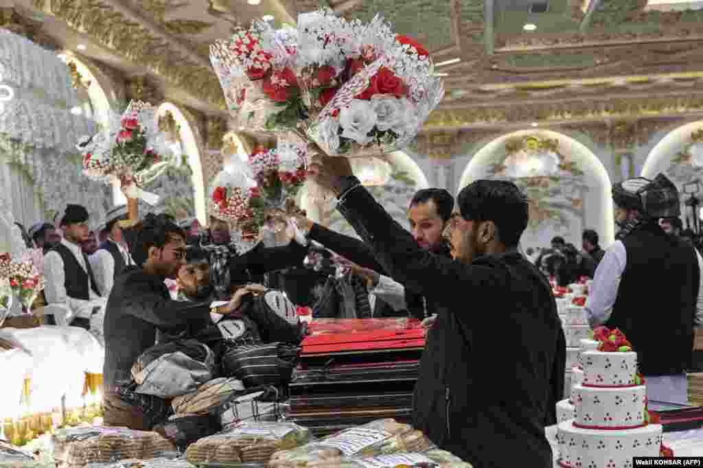 Voluntari afgani dau buchete de flori mirilor, în timpul unei ceremonii de nuntă în masă la o sală de nunți din Kabul.