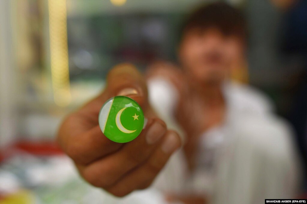 A vendor shows an ear clip of the national flag. Pakistani Prime Minister Shehbaz Sharif and opposition leader Raja Riaz agreed on August 12 to name Senator Anwaar-ul-Haq Kakar as caretaker premier to oversee elections, the prime minister&#39;s office said.