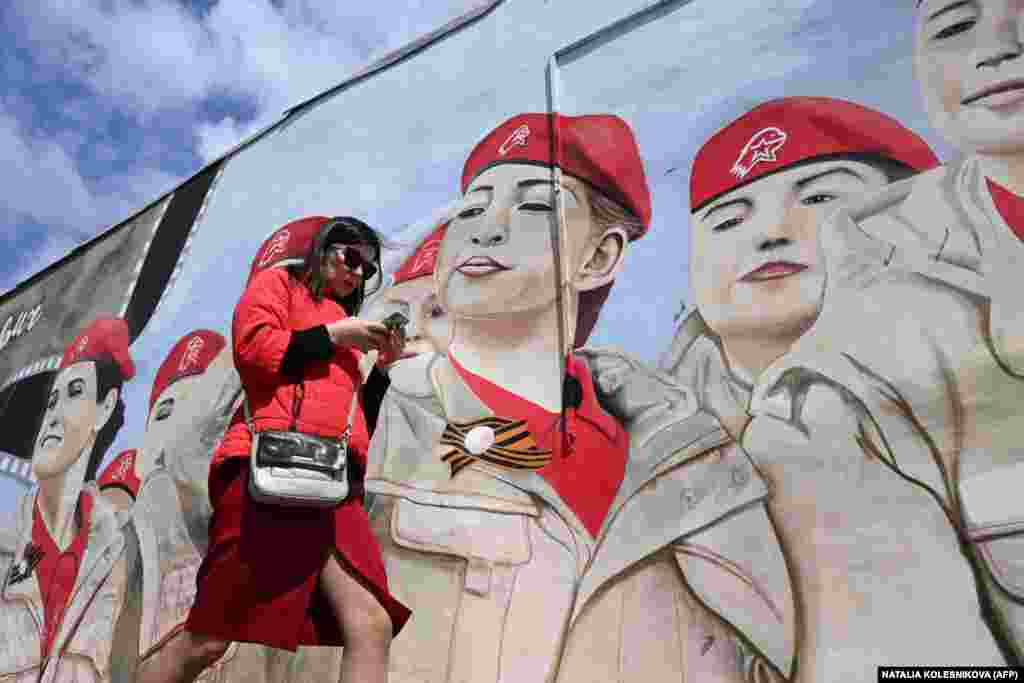 A woman uses her smartphone while walking past a mural depicting members of Russia&#39;s Yunarmia (Young Army) youth patriotic movement in Moscow.&nbsp;