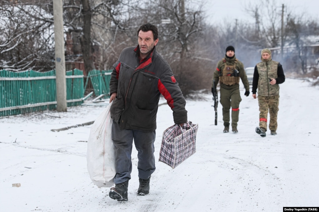 Një banor duke ecur nëpër një periferi të Avdivkas ndërsa pas tij janë dy ushtarakë rusë, më 19 shkurt 2024. Teksa forcat ruse rrethuan Avdivkan në shkurt, shumë nga banorët e mbetur u detyruan të largohen. Mbetet e paqartë se sa kanë mbetur.