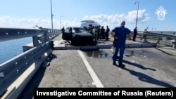 Anchetatori ruși și membri ai serviciilor de urgență adună probe lângă o mașină distrusă pe secțiunea avariată a podului, la 17 iulie.