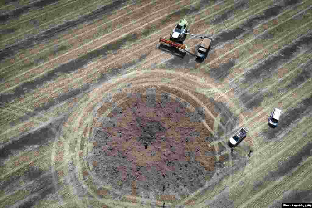 Фермери збирають урожай навколо вирви, яку залишила після себе російська ракета на полі у Дніпропетровській області. Фото від 4 липня 2023 року