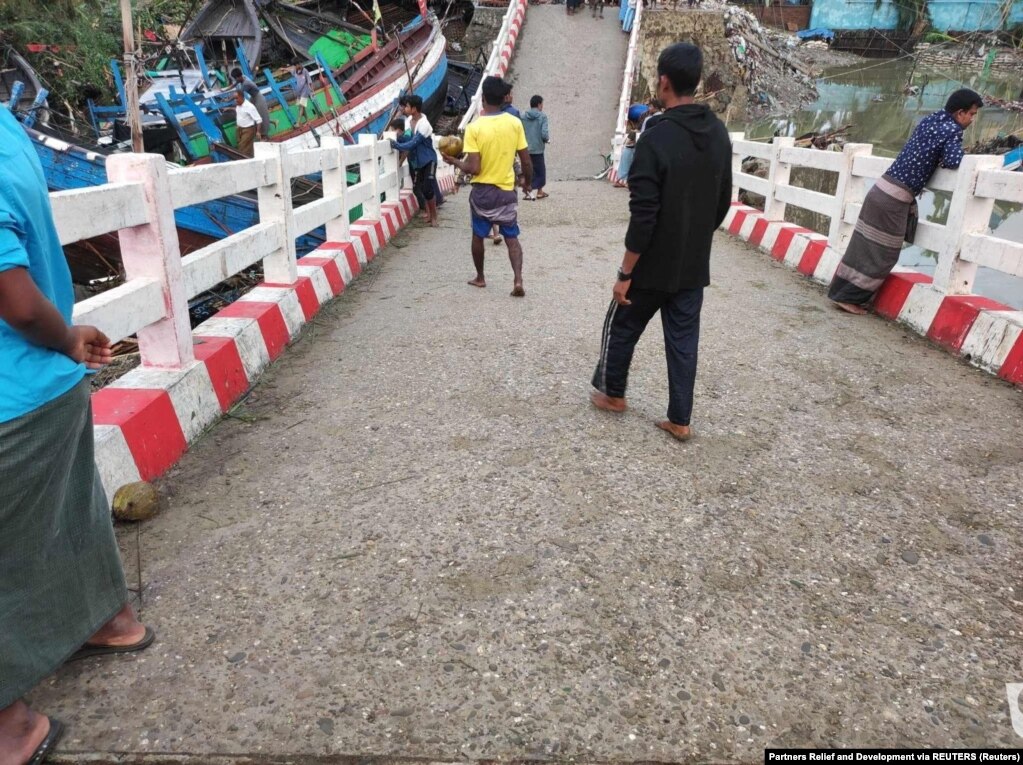 Njerëzit duke ecur mbi një urë të thyer si pasojë e ciklonit Mocha në Sitve, Mianmar.