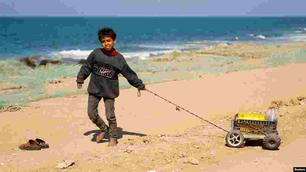 Raseljeno palestinsko dijete, koje je pobjeglo zbog izraelskih napada, vuče mala kolica s nekoliko flaša vode na obali mora u Rafi, 20. februara 2024.