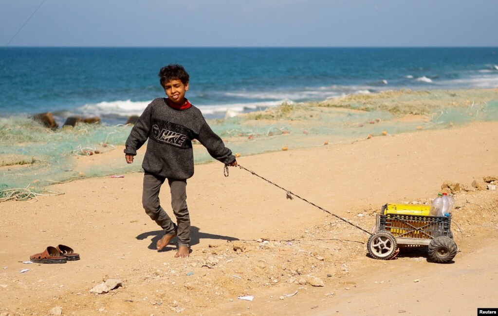 Një fëmijë palestinez i zhvendosur, i cili iku për shkak të sulmeve izraelite, tërheq një karrocë të vogël me disa shishe për ujë, pranë bregut të detit në Rafah,&nbsp; 20 shkurt 2024.