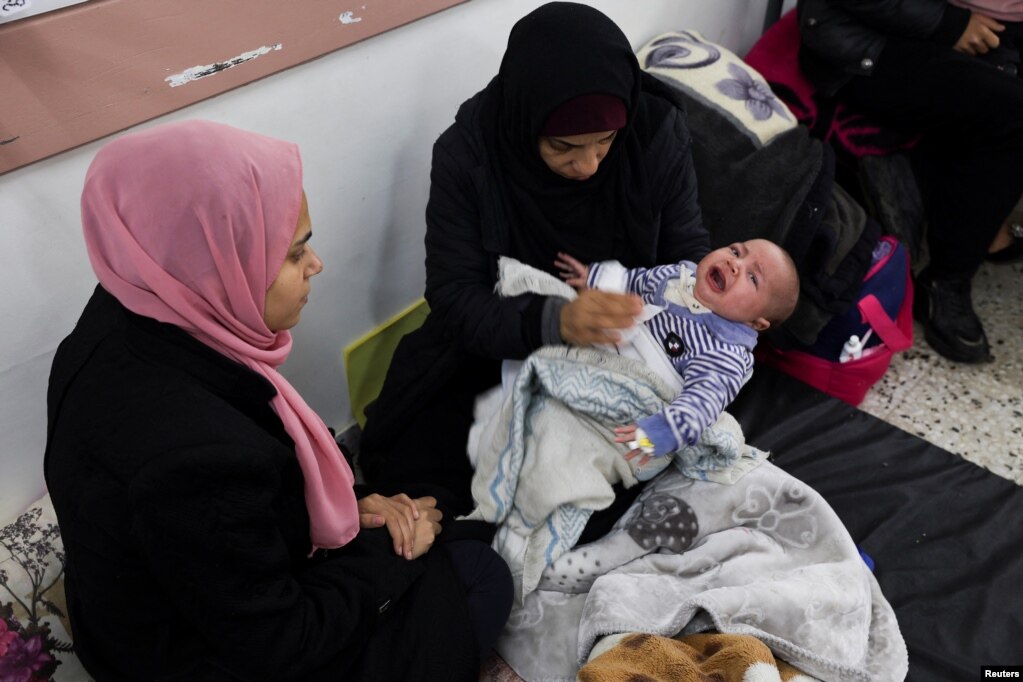 Një grua palestineze mban një fëmijë teksa presin ekzaminimin nga një mjek në një qendër shëndetësore në Rafah, 20 shkurt 2024. Përhapja e shpejtë e sëmundjeve është kryesisht për shkak të mbipopullimit dhe higjienës së dobët të shkaktuar nga mungesa e tualeteve dhe ujit për larje.